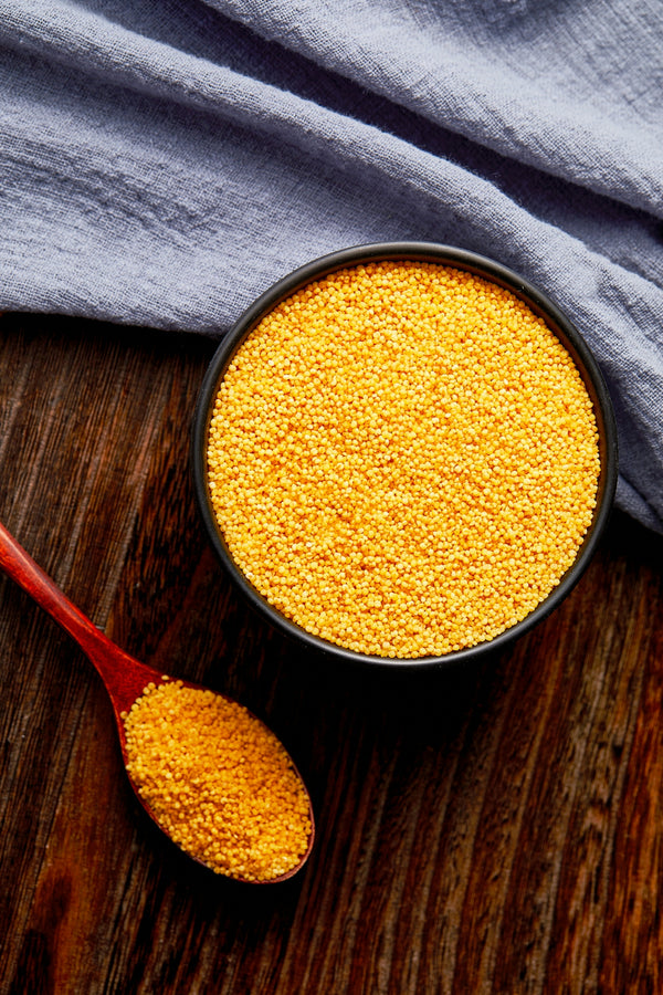 a bowl of mustard next to a spoon on a wooden table